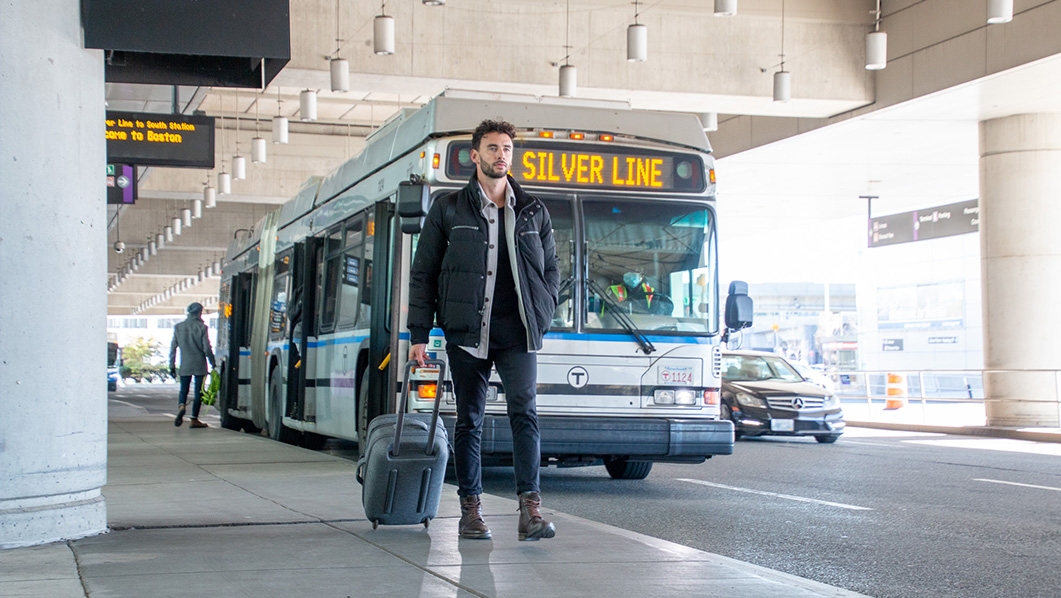 Man walking with suitcase and bus in background