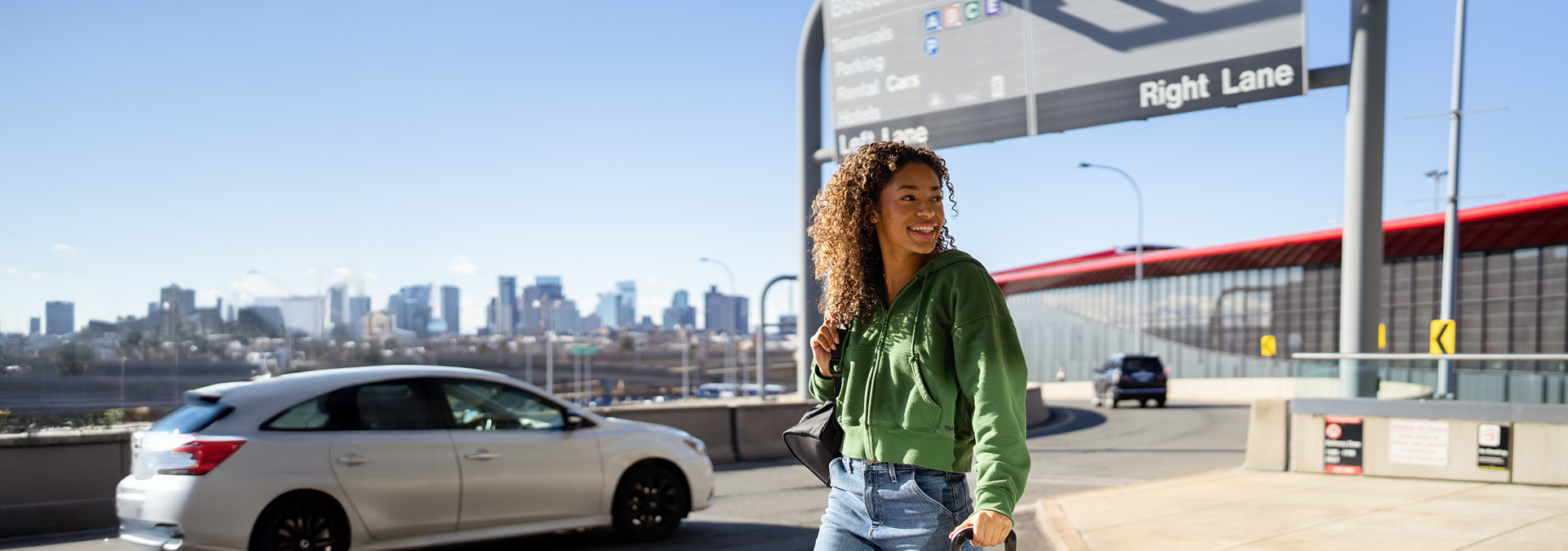 Girl with luggage walking outside terminal E with Boston skyline in the background