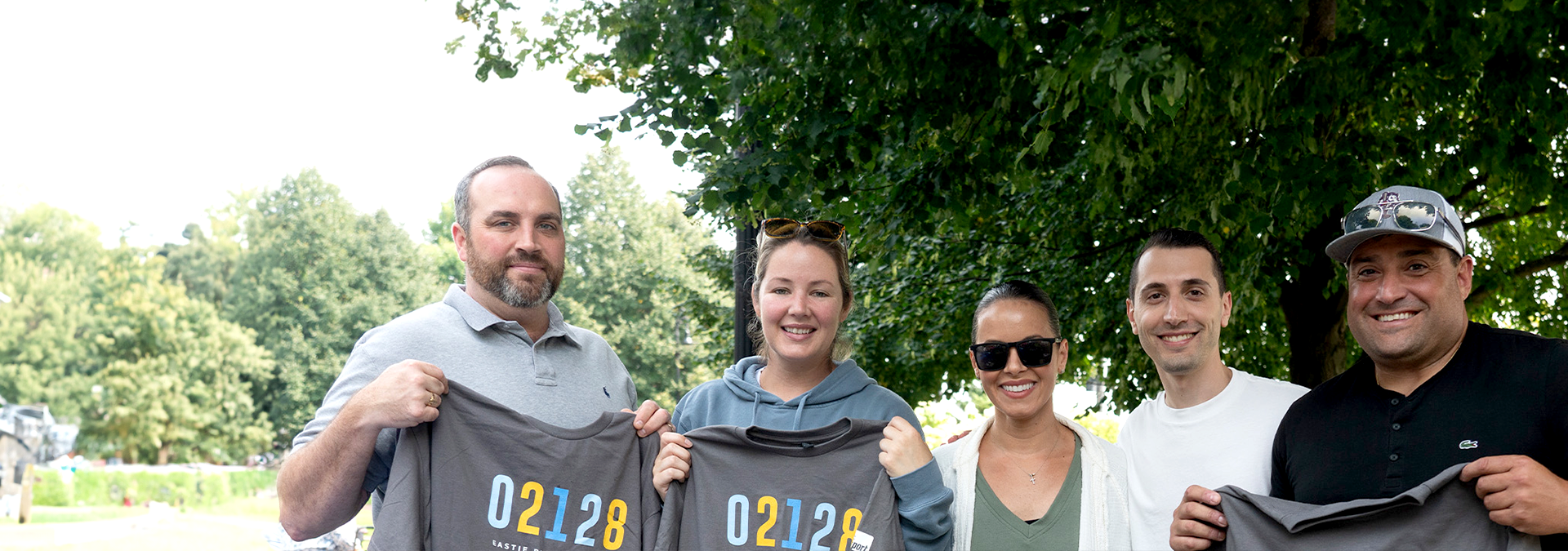 Massport Community Team at Eastie Pride event holding up t-shirts outside on a sunny day